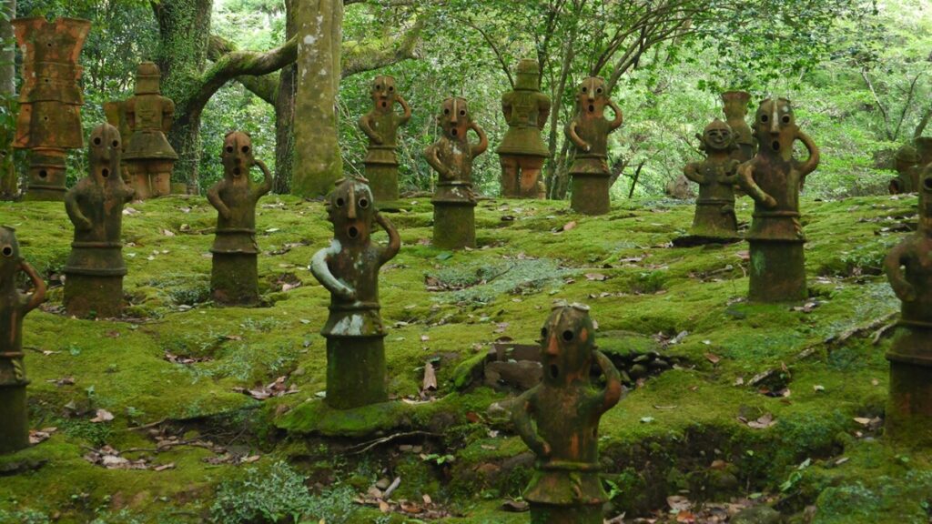 variety of haniwa clay figures surrounded by green scenery: trees, rocks with moss, and leaves. 
